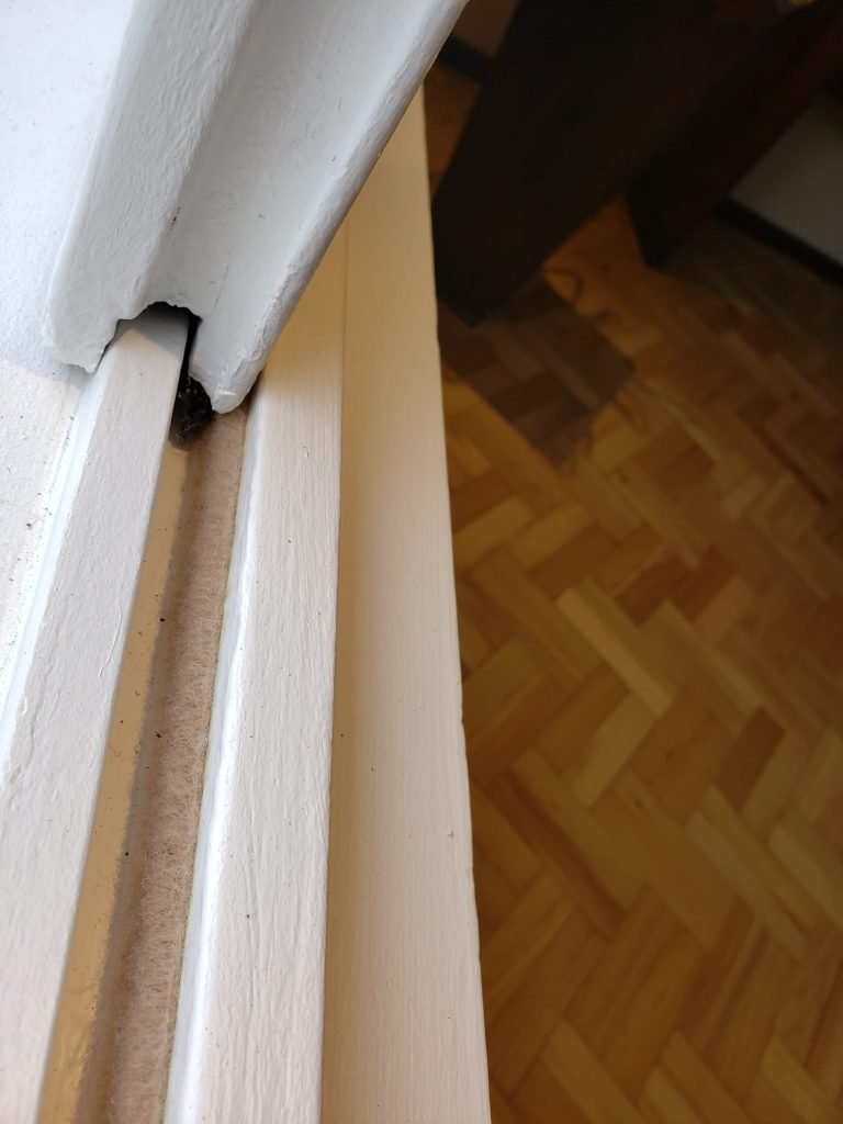 Ventana corrediza de madera en color blanco. En el zócalo abierto se ve un burlete de fieltro color beige.