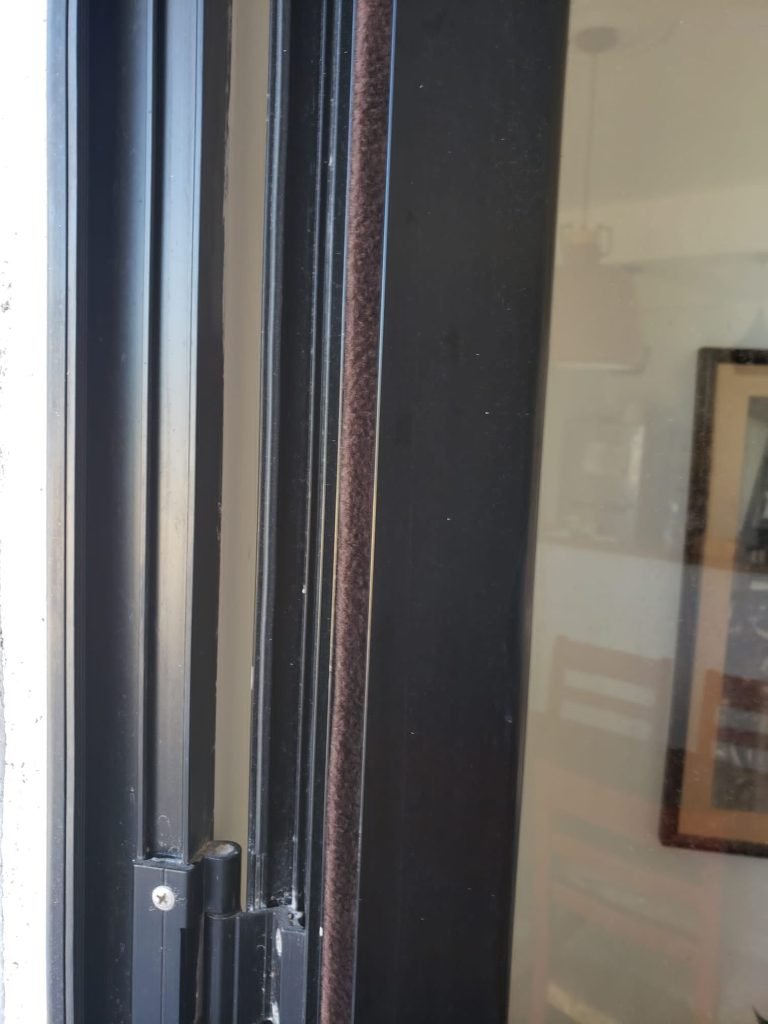 Puerta de aluminio, de vidrio, con marco color negro, con bisagras y la instalación en su junta de burlete de fieltro color marrón rojizo