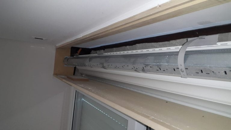 Interior de un cajón de madera de una persiana de PVC en una ventana de aluminio, aislado con un burlete de goma.