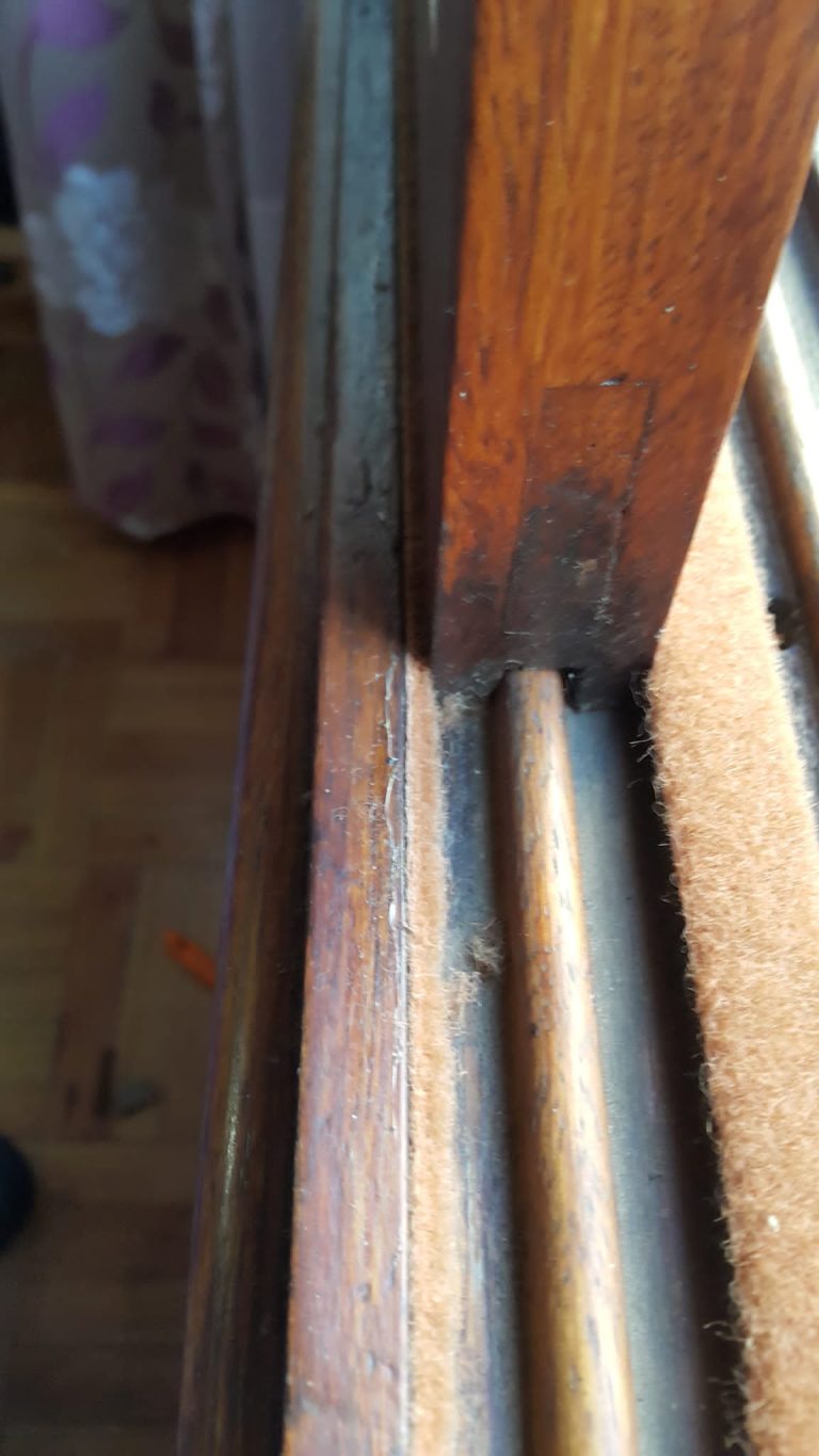 Ventana de madera barnizada abierta. La imagen muestra la ventana corrediza con doble aislamiento: burletes de fieltro naranja claro entre las dos partes de la ventana y entre la ventana y los marcos. La eficacia del aislamiento es visible en todos los puntos de contacto.